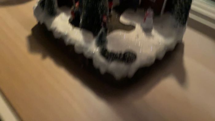 Ett juldekorerat miniatyrlandskap med snö, träd, en snögubbe och miniatyrfigurer.