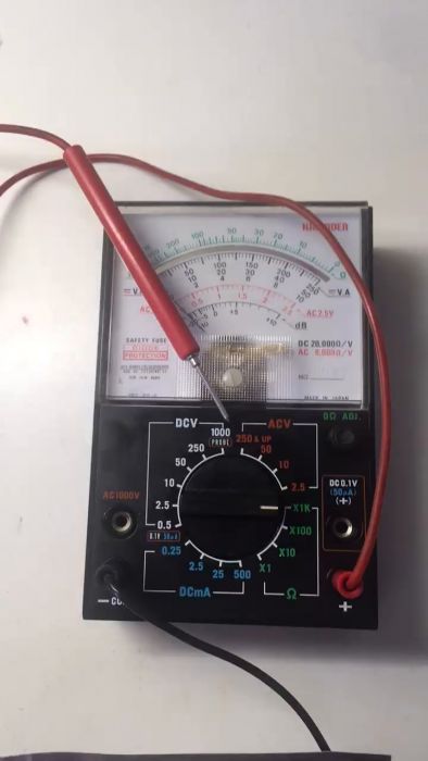 En analog multimeter med röda och svarta testledningar. Mätarens skala och reglage syns.
