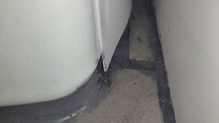 En film av en toalettstol nära ett golv, med en smutsig ansamling runt basen och fogarna.