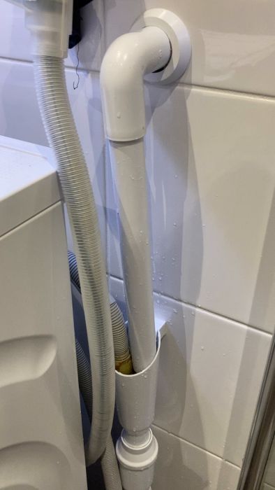 Filmen visar ett vitmålat avloppsrör och en flexibel avloppsslang från en tvättmaskin, mot kaklade väggar med vattendroppar synliga.