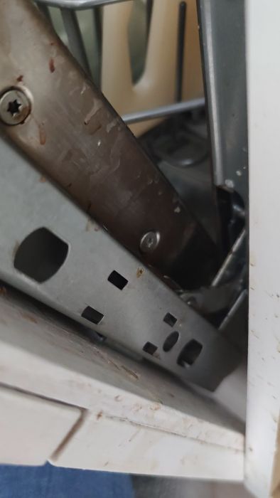 Inuti en uppvaskmaskin, detalj av bestickkorg och täta metallkomponenter, med tecken på vattenfläckar och användning.
