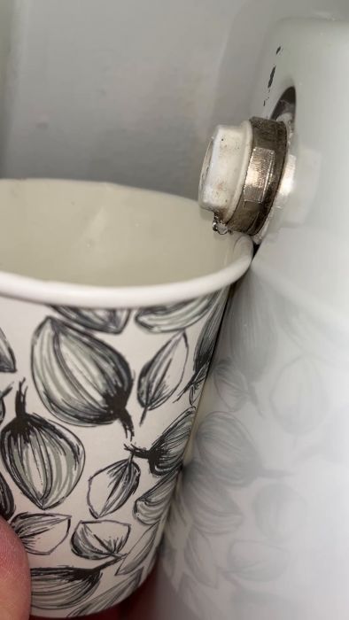 Ett mönstrat kaffekopp hålls nära en vattenkokare, där ånga strömmar ut och värmer koppen.