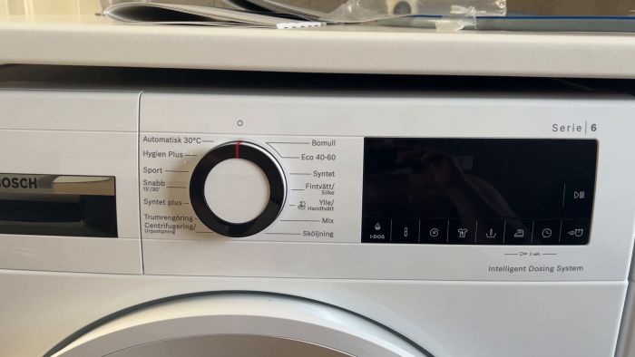 En tvättmaskins kontrollpanel med olika programval och inställningar på en digital display.