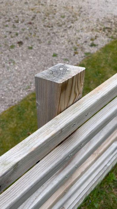 Ett trästaket med en stolpe, närbild. Grönt gräs och grus i bakgrunden. Fokus på stolptoppen.