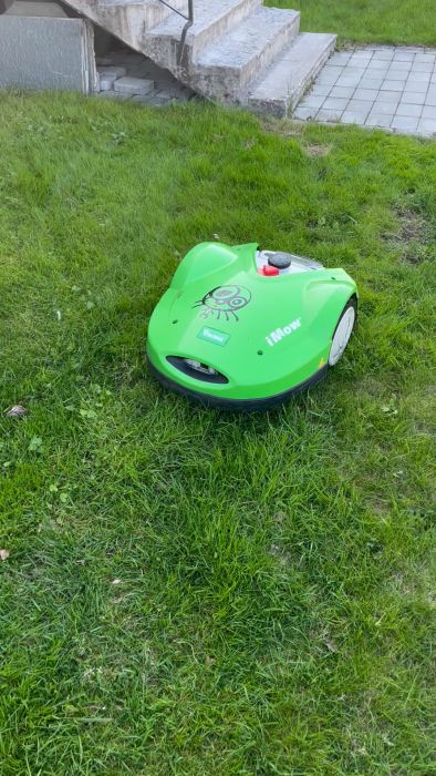 En grön robotgräsklippare på gräset nära en betongtrappa och grå plattor.