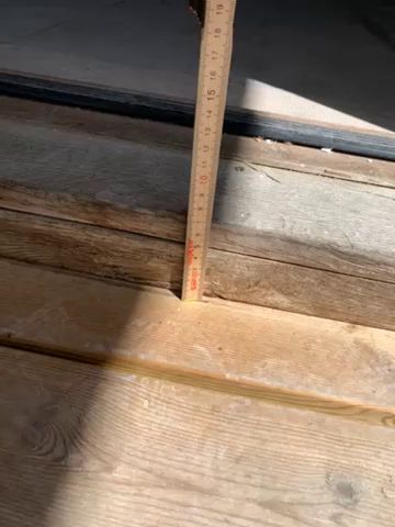 Ett tak i en byggnad där delar av det vita paneltaket är borta, vilket avslöjar de underliggande träbjälkarna och en orörd del av korridoren.