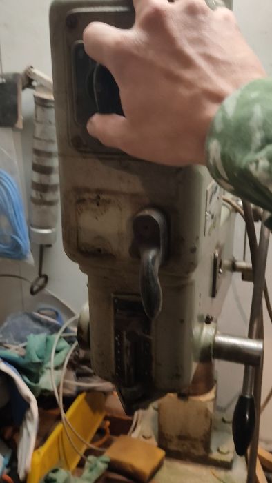 En bänkmonterad pelarborr i en verkstad med saker runtomkring, som ser använd och smutsig ut.