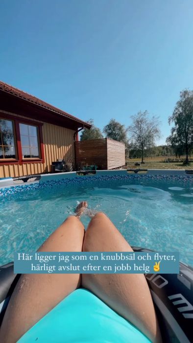 En person slappar i en pool med hus och klarblå himmel i bakgrunden. Text i filmen ger en avslappnad och positiv känsla.