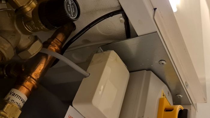 VVS-inställningar och en vit behållare under en vit strukturerad yta, med svarta och vita kablar och rör.