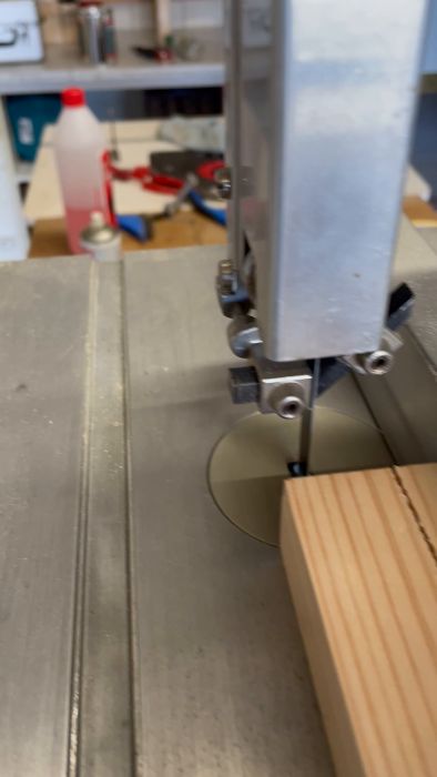 En sågmaskin skär en spår i en träplanka. Sågspån och arbetsbänk syns.