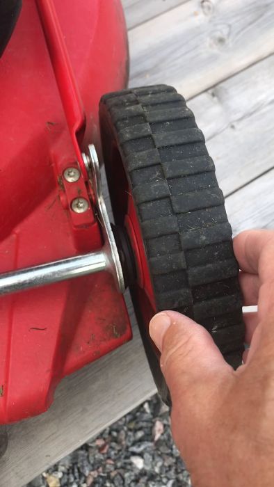 En person använder en tång för att fixa ett hjul på en röd gräsklippare.