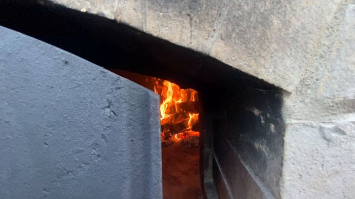 Eld flammar upp inne i en metallstruktur, möjligtvis en ugn eller en kamin med öppen lucka eller dörr.