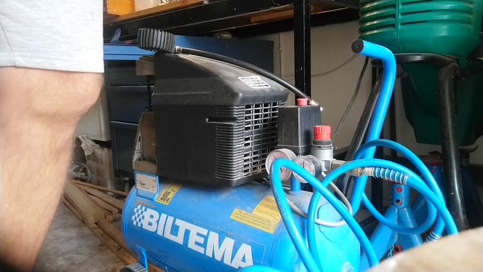 En luftkompressor märkt "#BILTEMA" med manometer och slangar i ett rörigt garage.