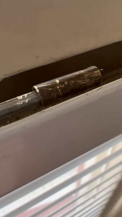 En närbild på ett nedsmutsat fönsters säkerhetsspärr av metall med damm och spindelnät i en vardaglig miljö.