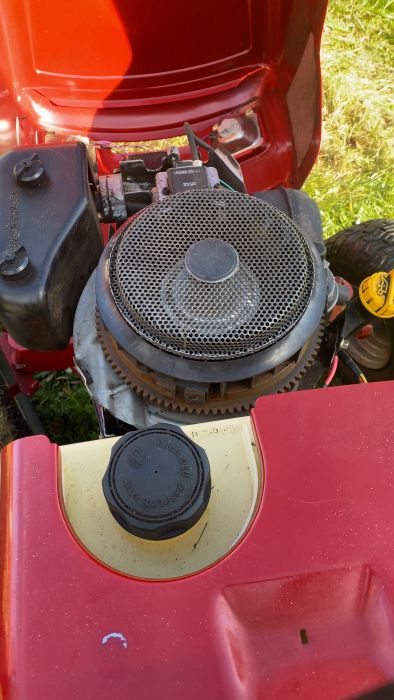 En närbild av en röd gräsklippare med öppen motorhuva som visar motorn och några plastkomponenter.