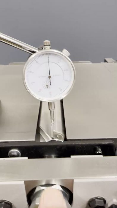 Ett mätdon, troligen en urtavla indikator, mäter precision på en maskin eller komponent. Metalliskt grått och vit bakgrund.