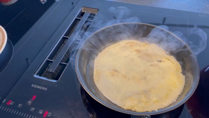 En stekpanna på en Siemens induktionshäll med en brummande pannkaka; ånga stiger upp vid tillagning. Cupsynlig i vänster hörn.