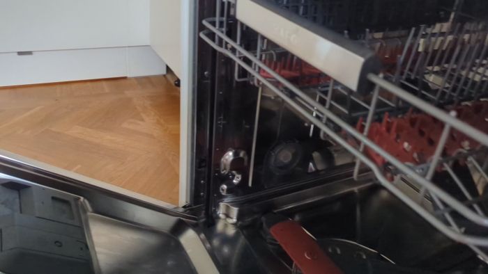 Öppen diskmaskin visar inre mekanismer och underhållsarbeten, med metallpaneler och synliga skruvar, mot en parkettgolv bakgrund.