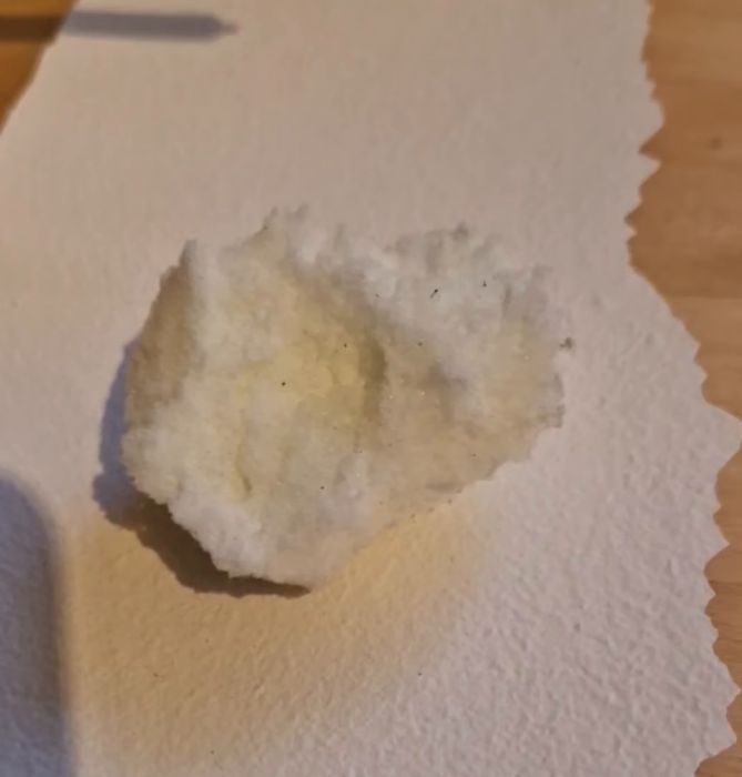 Ett pappersark med en vit, fluffig substans på, och en pincett som klämmer tag i den.