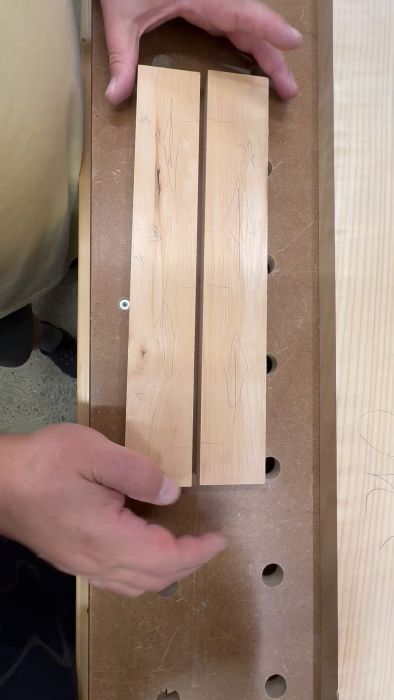 Händer placerar ett trästycke med markerade linjer på en arbetsbänk med hål. Verkar förbereda för snickeri eller träbearbetning.