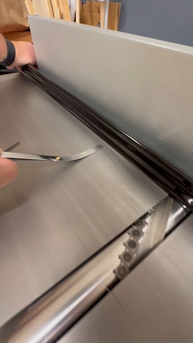 En person reparerar en glidande dörrskärm med en skruvmejsel. Det är en närbild av handen och verktyget i arbete.