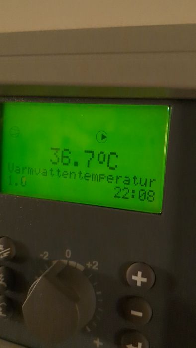 Digital termometer visar 36.7°C. Texten under indikerar "Varmvattentemperatur". Panel med knappar och reglage syns nedanför.