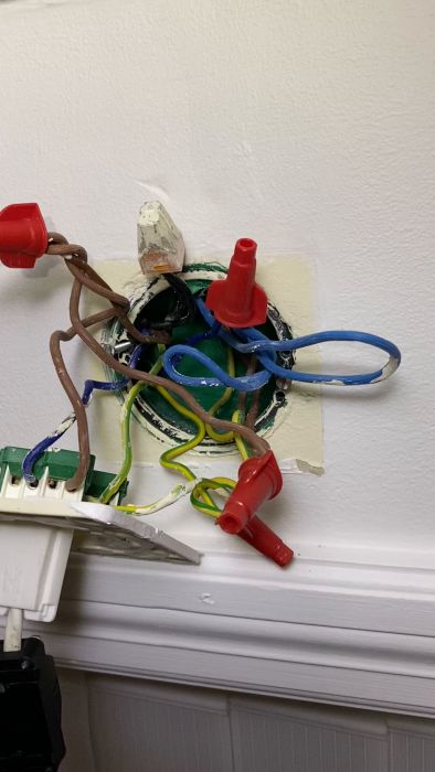 En elektrisk installation med färgglada kablar, kåpa, och en röd kabelsko. Verkar vara handhavandefel och potentiellt osäker.
