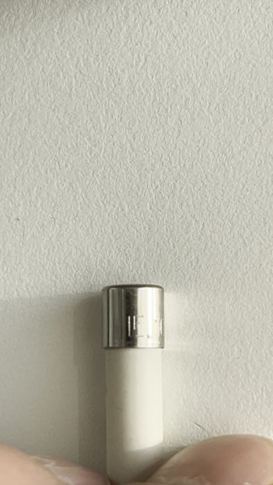 Hand håller en elektronisk apparat mot en texturerad, vit vägg. Enheten har ett hål eller märke på sidan.