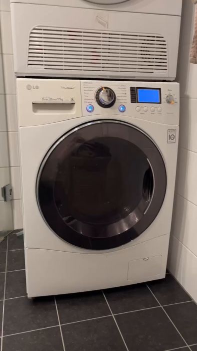 En vit LG tvättmaskin med frontlucka och elektronisk kontrollpanel i ett kaklat rum.