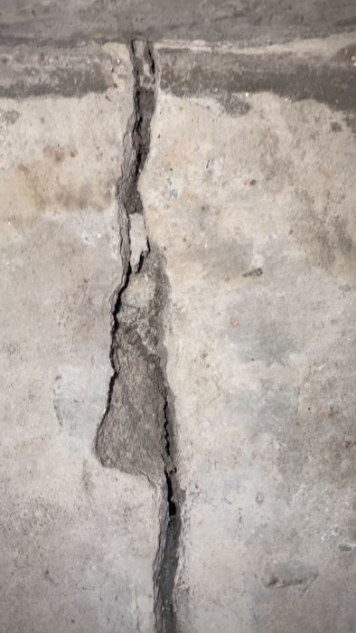 En spricka i en grå betongyta som går ojämnt vertikalt och tycks vara inspelad med belysning från höger sida.