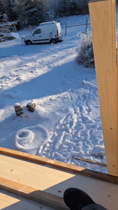 Träveranda som vetter mot en snöig trädgård med frostiga träd och äng under en klarblå himmel.