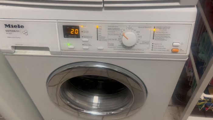 Detta är en vit främre tvättmaskinpanel av märket Miele Edition 111 med digital display och knappar för olika tvättprogram.