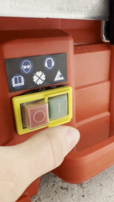 En hand trycker på en nödstoppknapp på en maskin med varningssymboler ovanför.