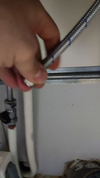 En person använder en skiftnyckel för att justera en metallventil på en rörinstallation, med vita plaströr och väggfästen i bakgrunden.