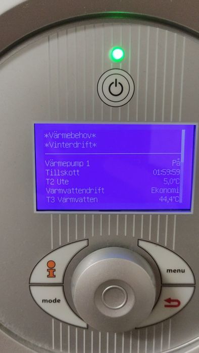 Ett finger justerar inställningar på en digital termostat med en LCD-skärm som visar temperaturer och driftslägen för en värmepump.