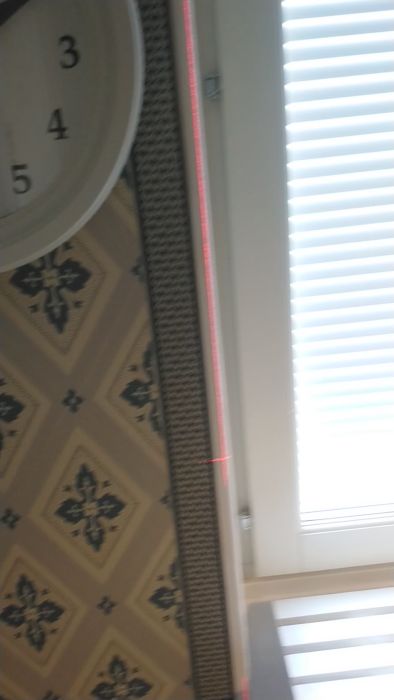 Detalj av tapetsering vid sidan av ett fönster, markerad med en lasermätare. Videon visar precisionen i mönsterpassning och hur lasern används för att säkerställa raka linjer vid fönsterramen.