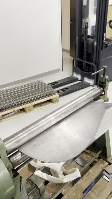 Se hur en aluminiumskiva bearbetas och formas till ett rör för en skorsten. Processen innefattar klippning, rundvalsning och svetsning, och utgör en del av ett större projekt för att bygga en säker takgenomföring för en kamin.